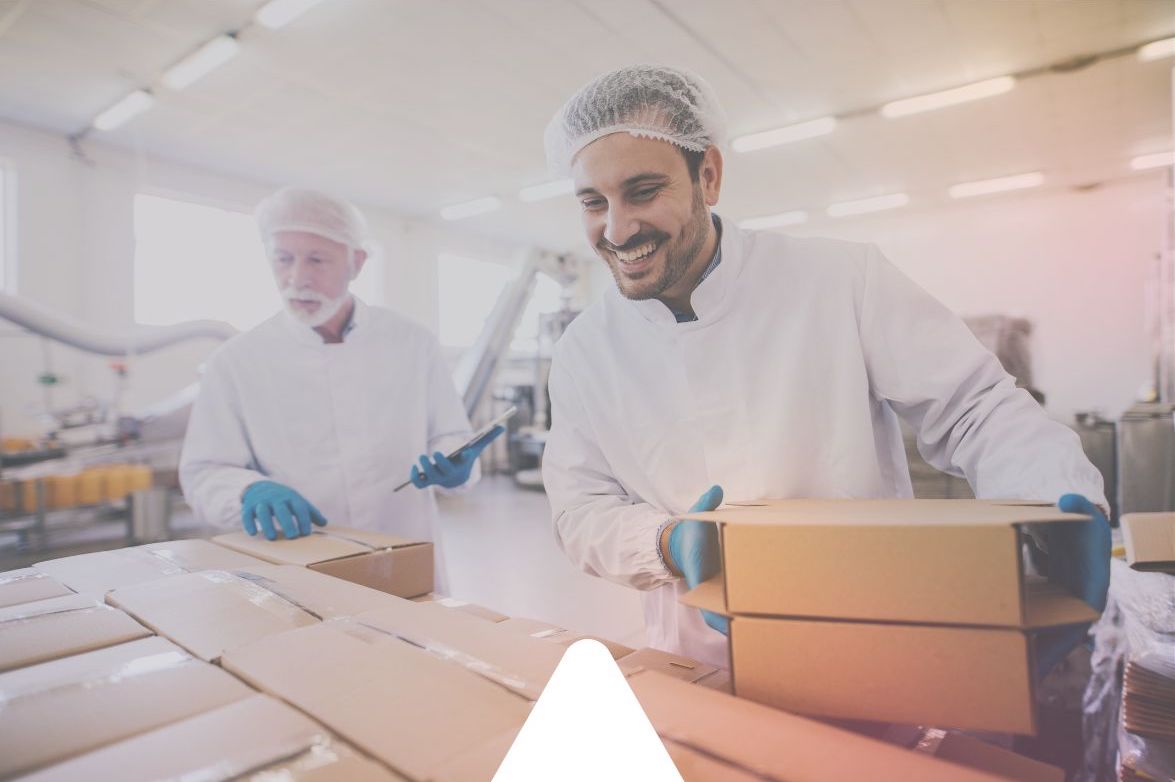 Two men in white safety coats and hair nets sort through delivery boxes as part of their safety processes