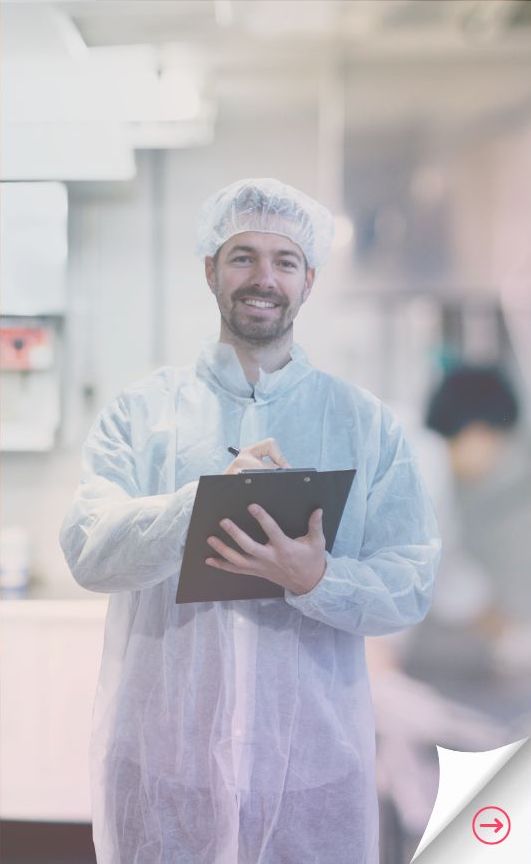 An Environmental Health Expert in a white safety coat and hair net writes on a clipboard