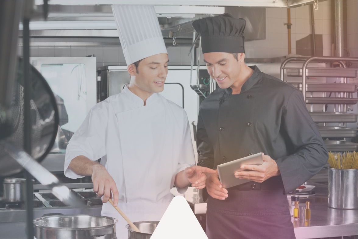 A chef and a kitchen manager, standing in a kitchen, look at a tablet with their safety solutions dashboard on