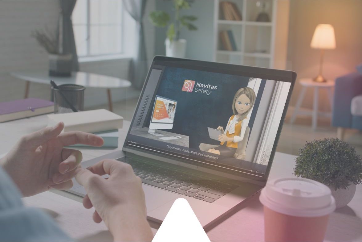 A person sits at a desk watching a laptop screen. On the screen is a Safety Training video